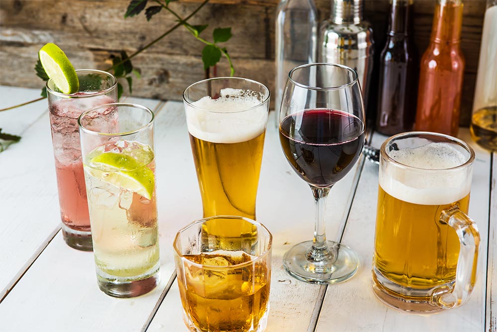 Foto: unterschiedliche Gläser mit alkoholischen und alkoholfreien Getränken stehen in loser Gruppe auf einem Tisch aus weißen Spuntbrettern